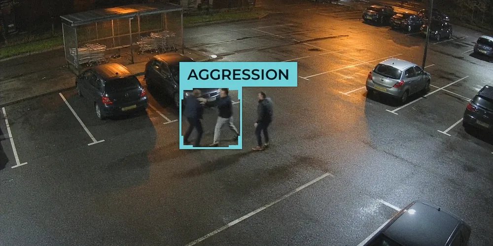 Night-time CCTV view of a retail car park with two men pushing each other and a third man approaching