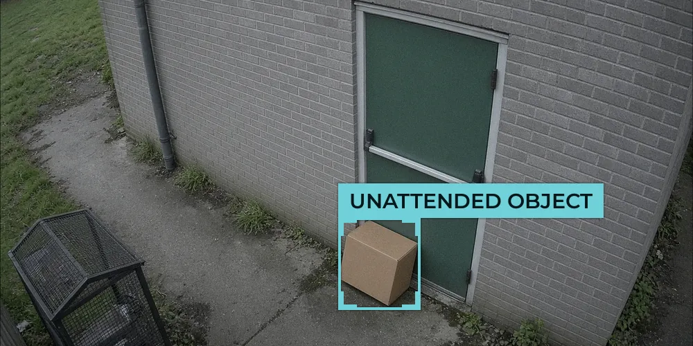 CCTV view of a cardboard box left against a green fire exit door at the side of a brick building